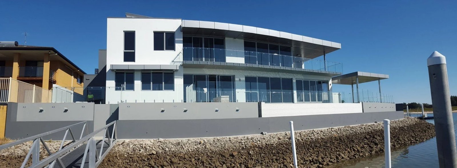 Modern waterfront home with frameless glass balustrade across two-storey balcony, installed by Harbour Glass
